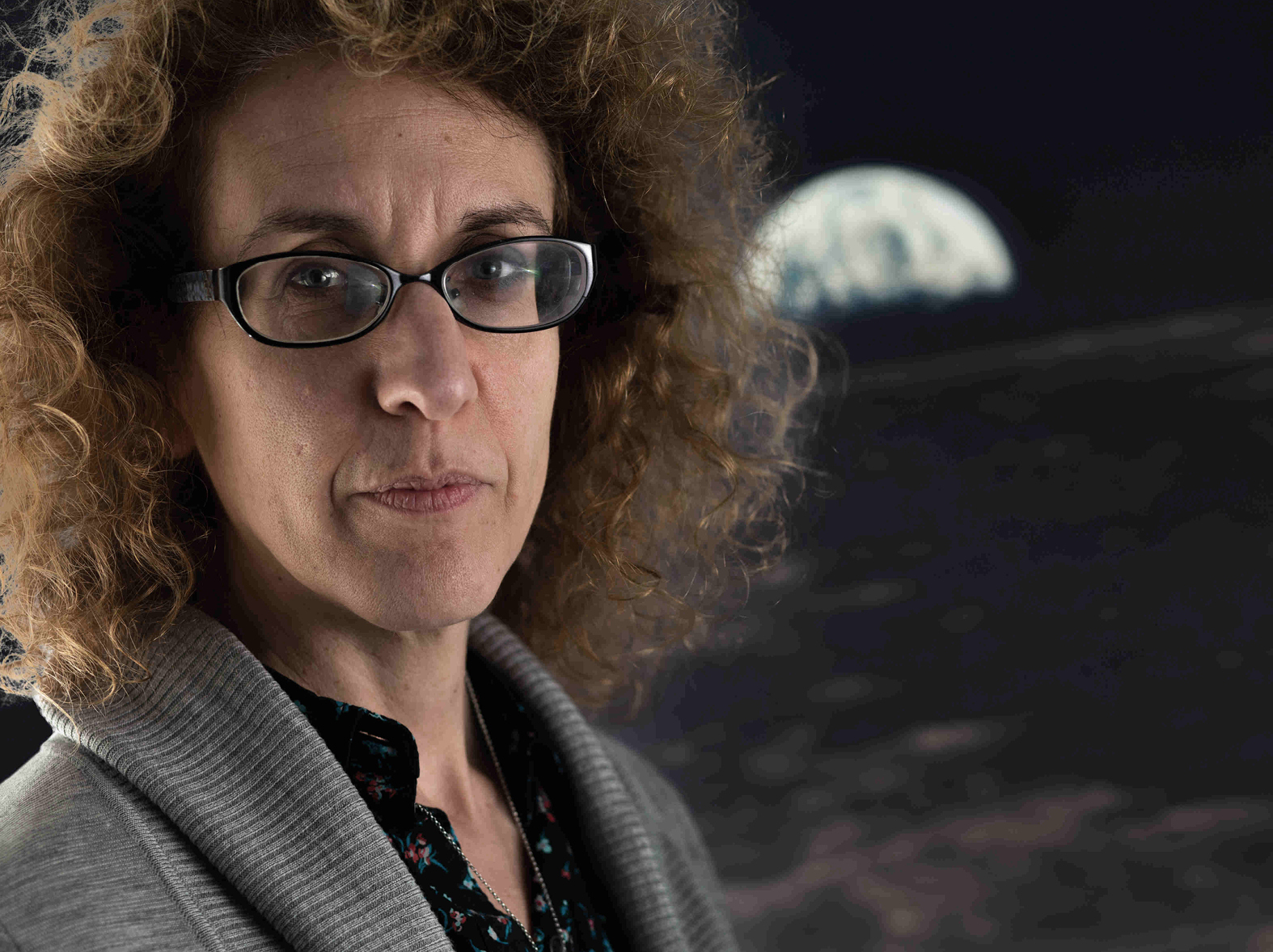 维姬·卡斯皮教授站在一张月球海报前看着镜头