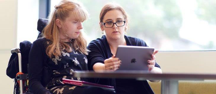 两个女人，一个坐着轮椅坐在笔记本电脑前